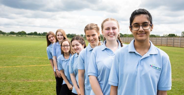 Row of school girls lined up behind each other on the playing field.