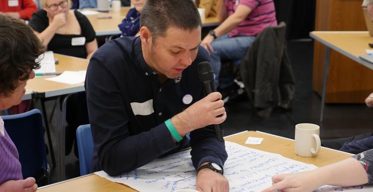 Man with a microphone reading off a large piece of paper.