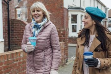 2 women walking outside talking and holding coffee