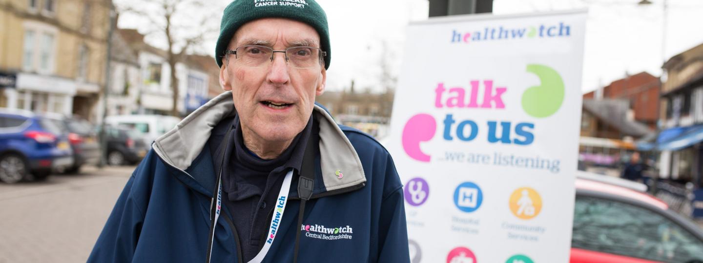 Male volunteer standing in front of a banner "Talk to us" 