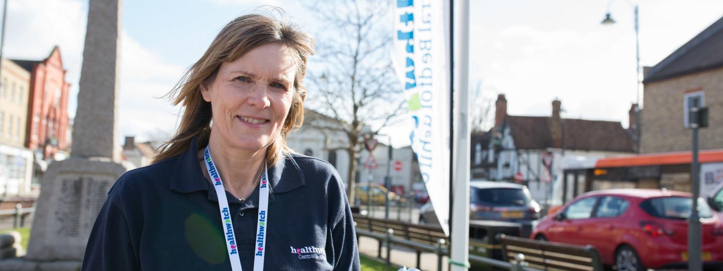 Healthwatch volunteer standing in front of a Healthwatch banner